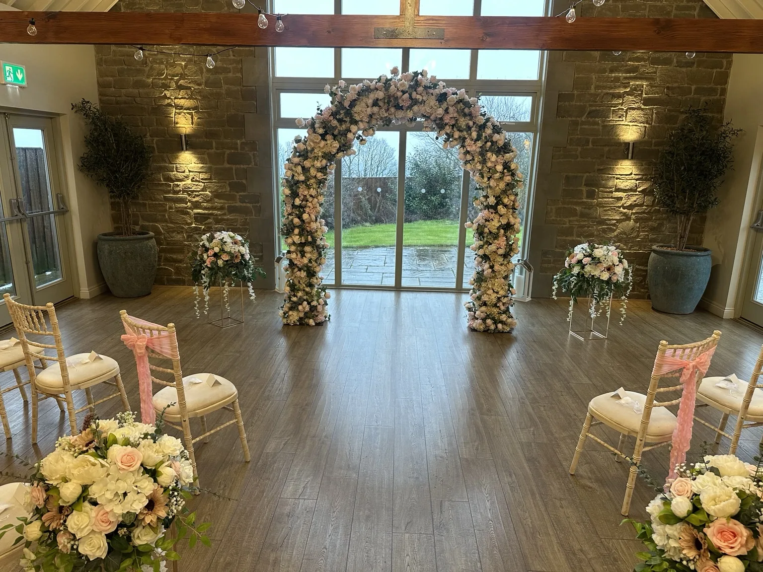 Clear full-height blush and ivory floral arch installed in a stone wedding ceremony room