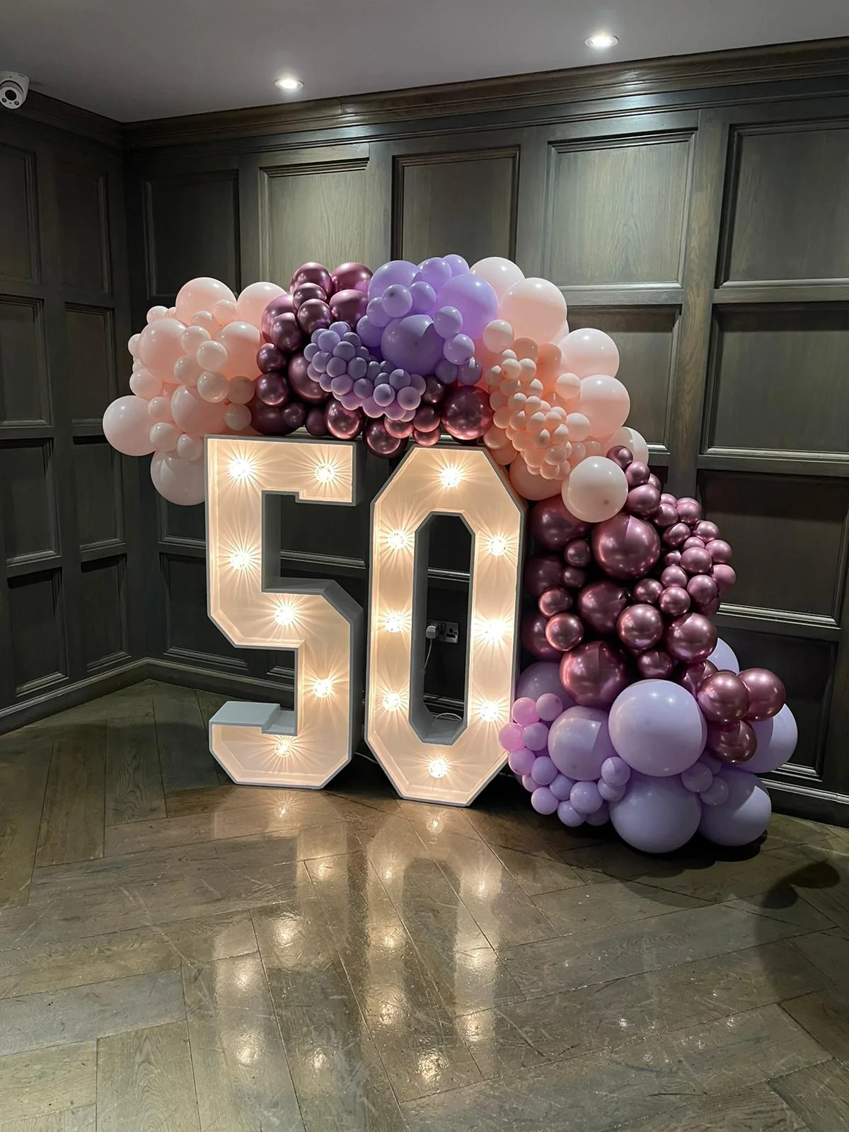 Large illuminated 50 numbers framed by pink and purple balloons for a milestone celebration